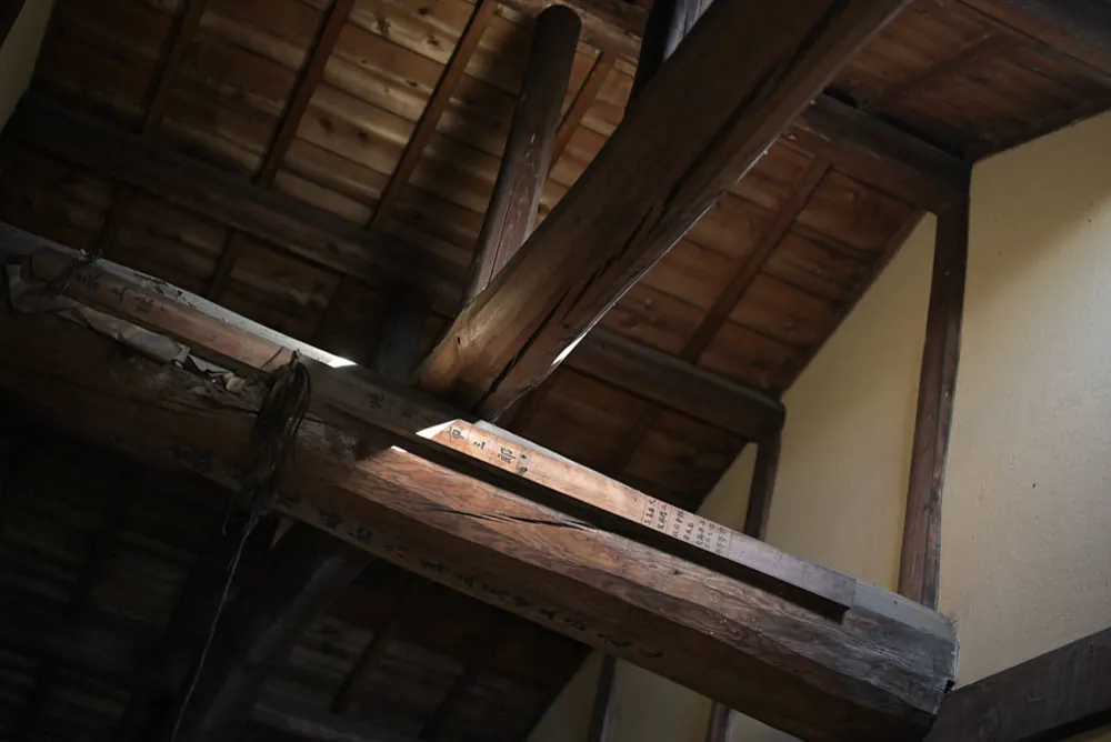 Heavy beams cross under the underside of the roof. Daylight catches one edge.
