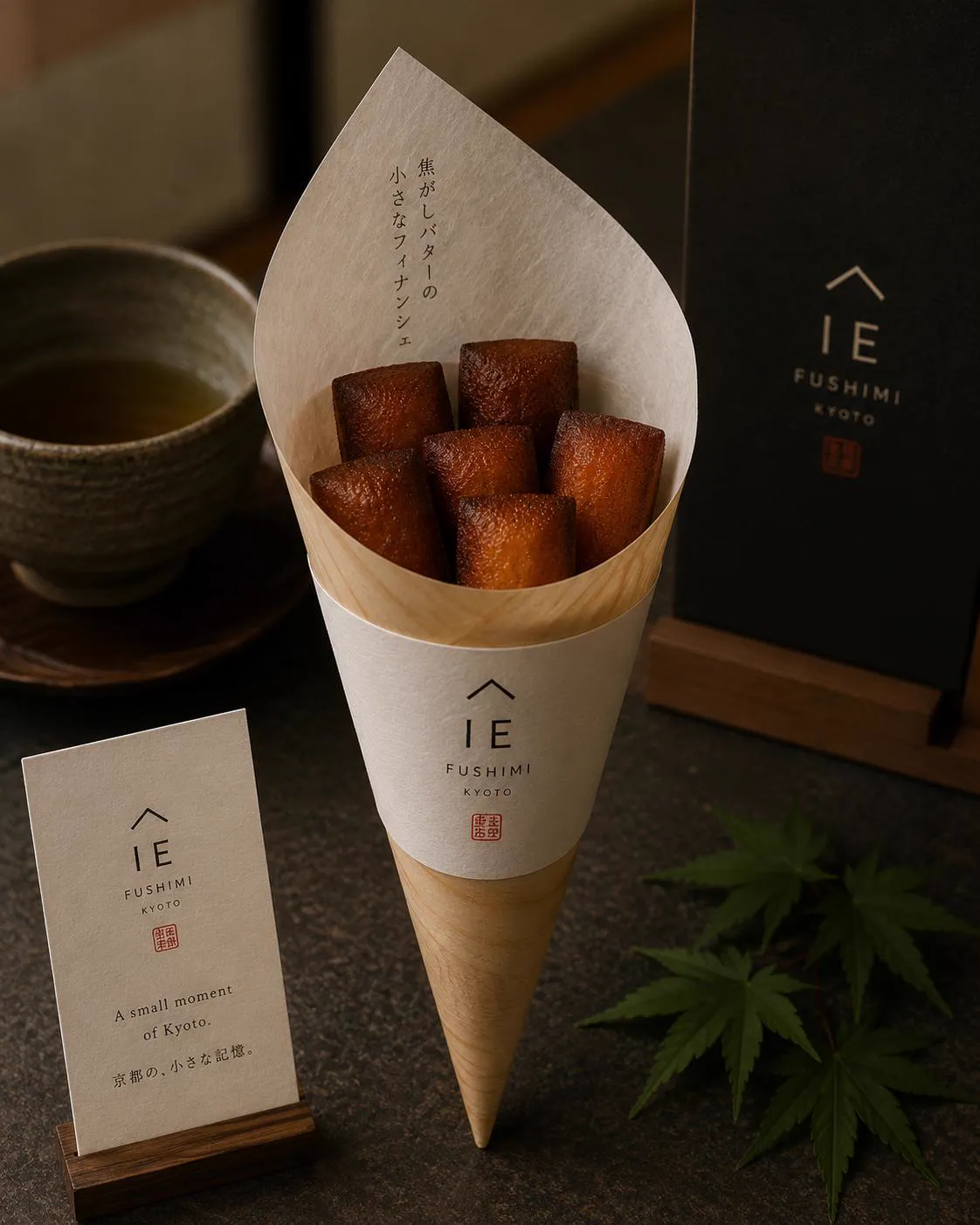 Brown butter financiers standing in a paper cone, a cup of tea beside them.