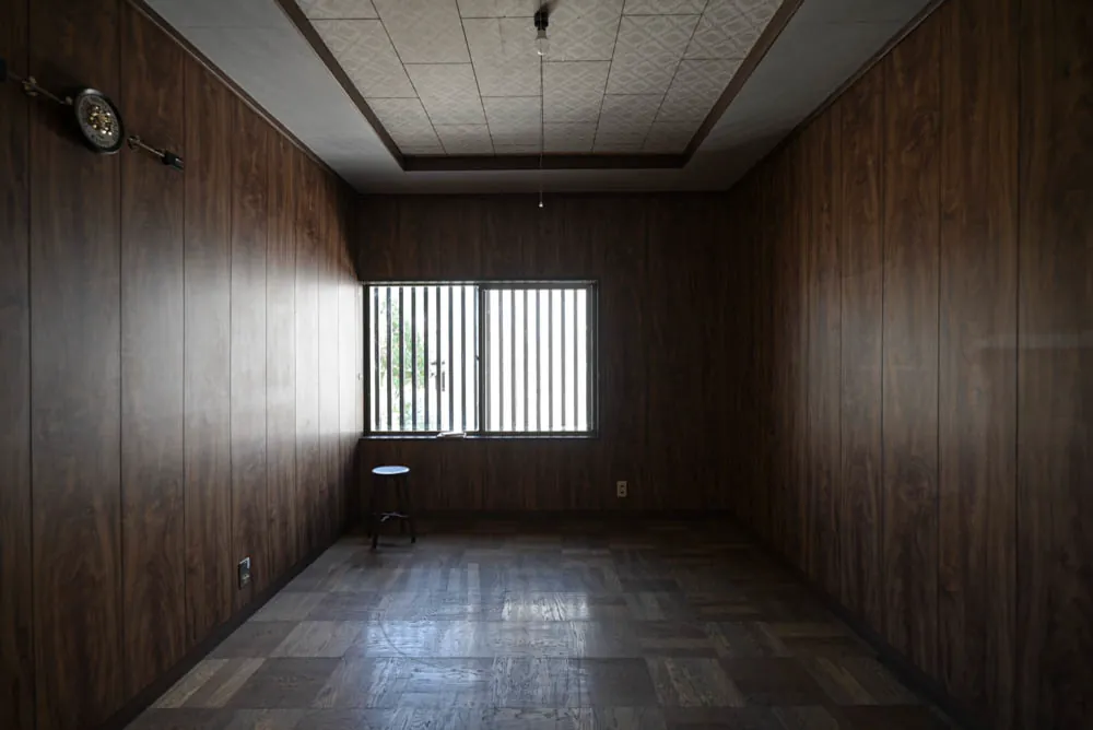 An upstairs room as found: panelled walls, a parquet floor, one window.