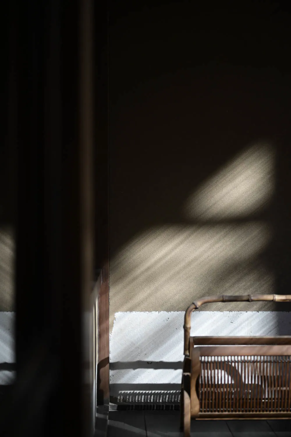 Sun across an earthen wall and an old cane chair.