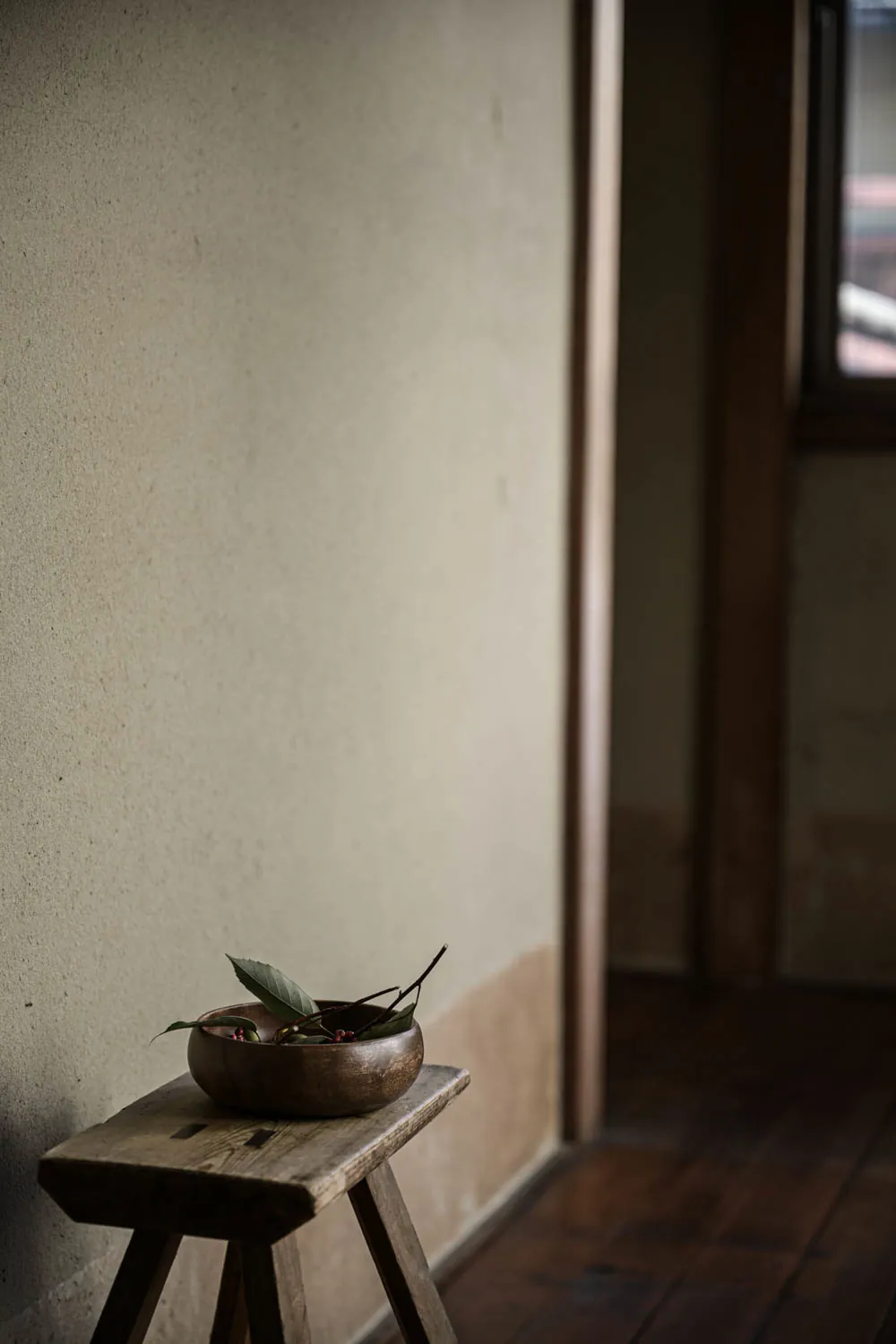 A worn wooden stool and a metal bowl against a plastered wall.