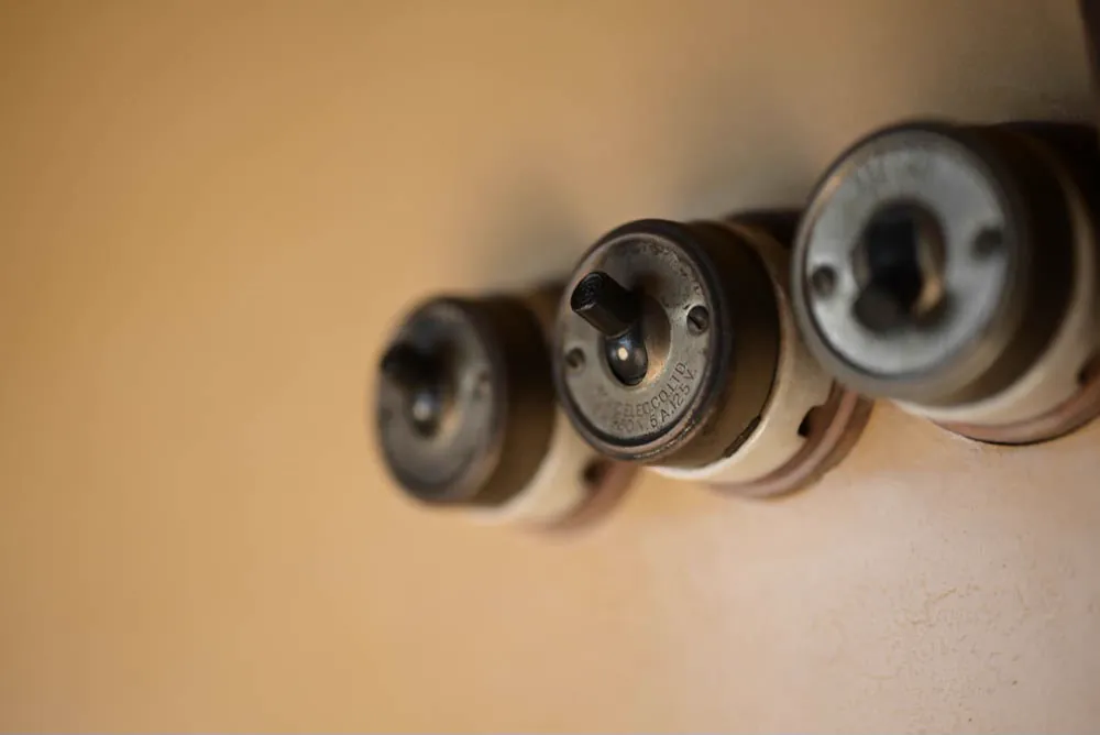 Three old rotary light switches on a plastered wall.