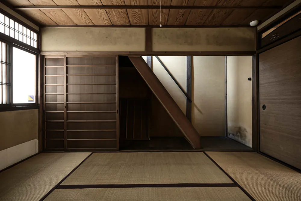 A tatami room with a steep wooden stair rising along one wall.