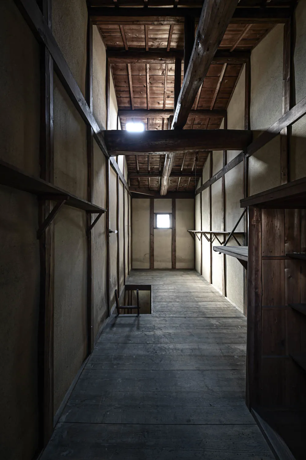 The long upstairs corridor: a log beam overhead, a skylight at the far end, bare floorboards.