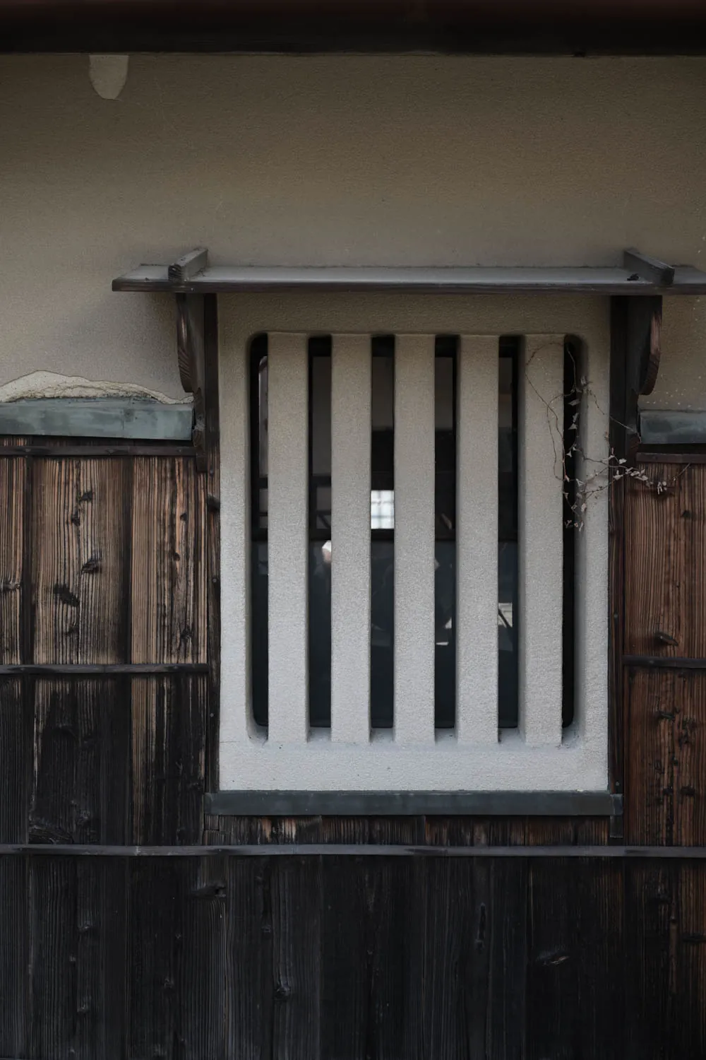 A plastered window with timber bars in a dark wooden wall.